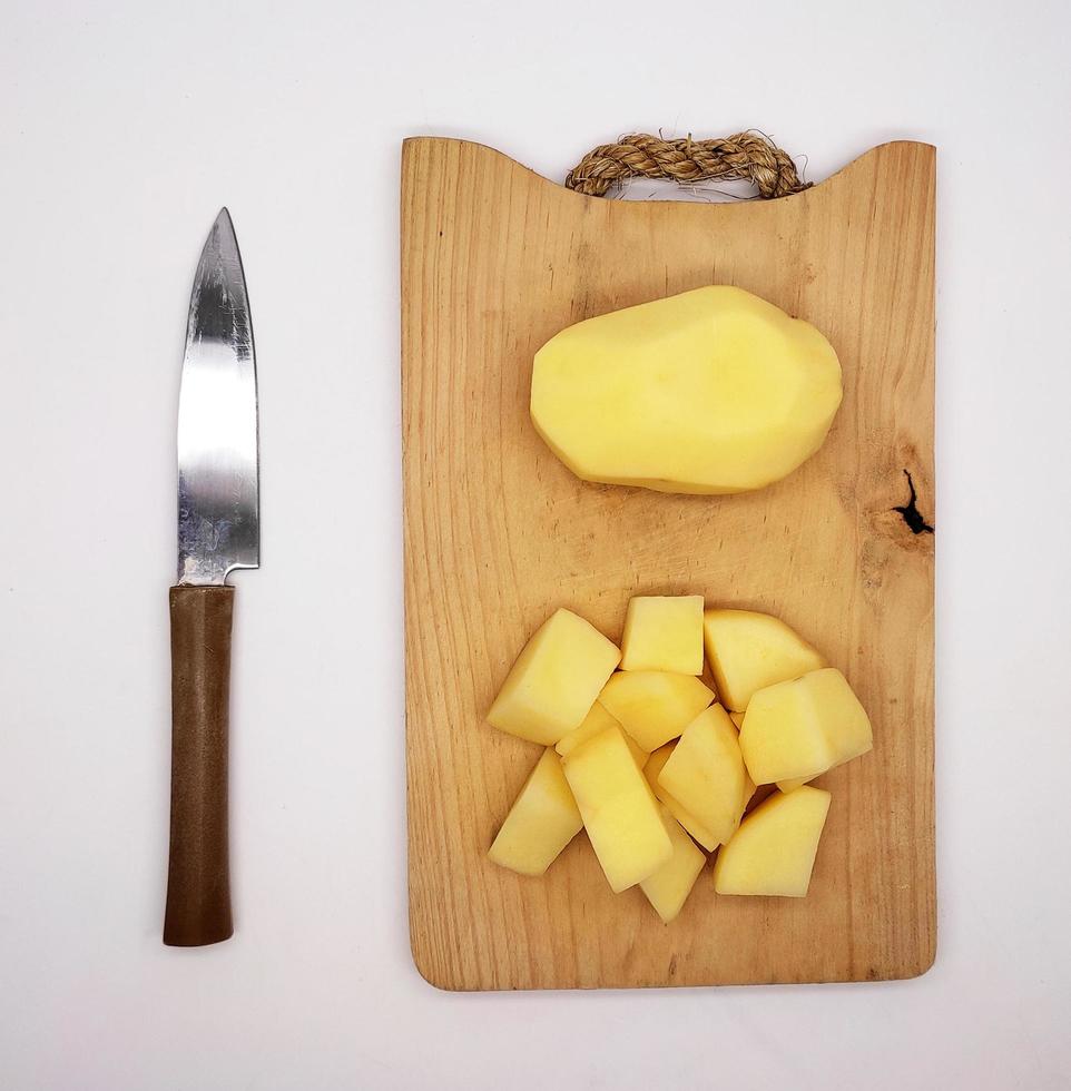 a dadini pelato patate e totale pelato patate, su un' di legno taglio asse, e un' cucina coltello. foto