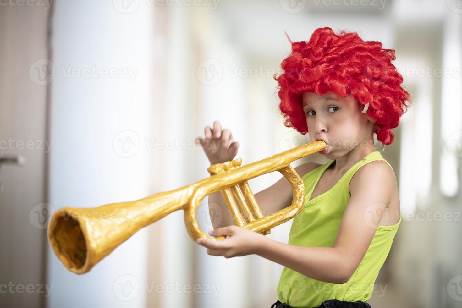 un' bambino nel un' luminosa parrucca giochi il tromba. divertente ragazzo con un' giocattolo musicale strumento. futuro artista foto