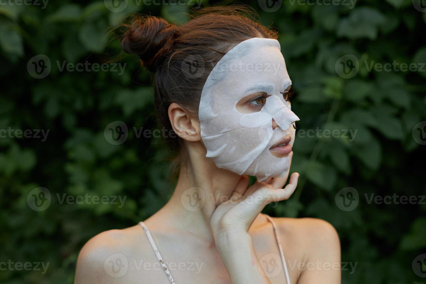 simpatico ragazza cosmetico maschera detiene il suo mano vicino il suo viso e sembra lontano spoglio le spalle le foglie nel il sfondo foto