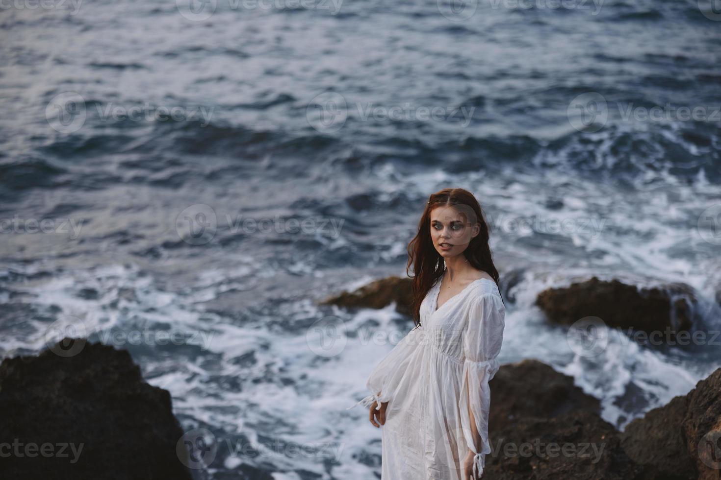 donna nel bianca vestito sta su un' scogliera stile di vita pietra costa paesaggio foto