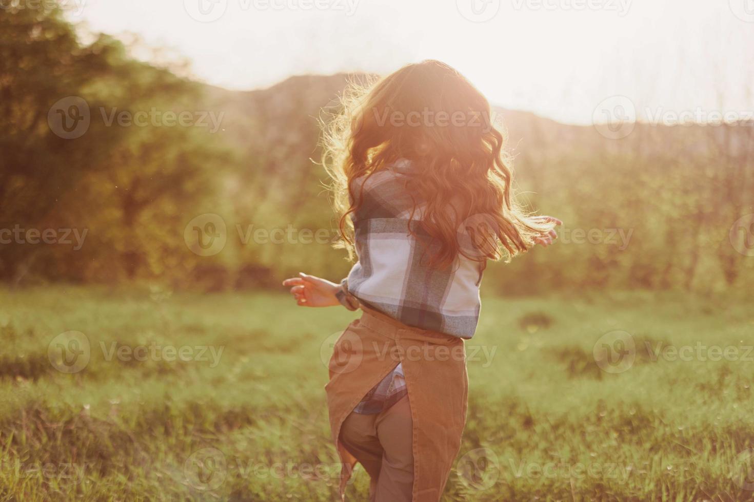 un' donna corre attraverso un' campo con sua indietro per il telecamera su un' estate giorno con sua capelli lungo e volante nel il tramonto. il concetto di la libertà e armonia con natura foto