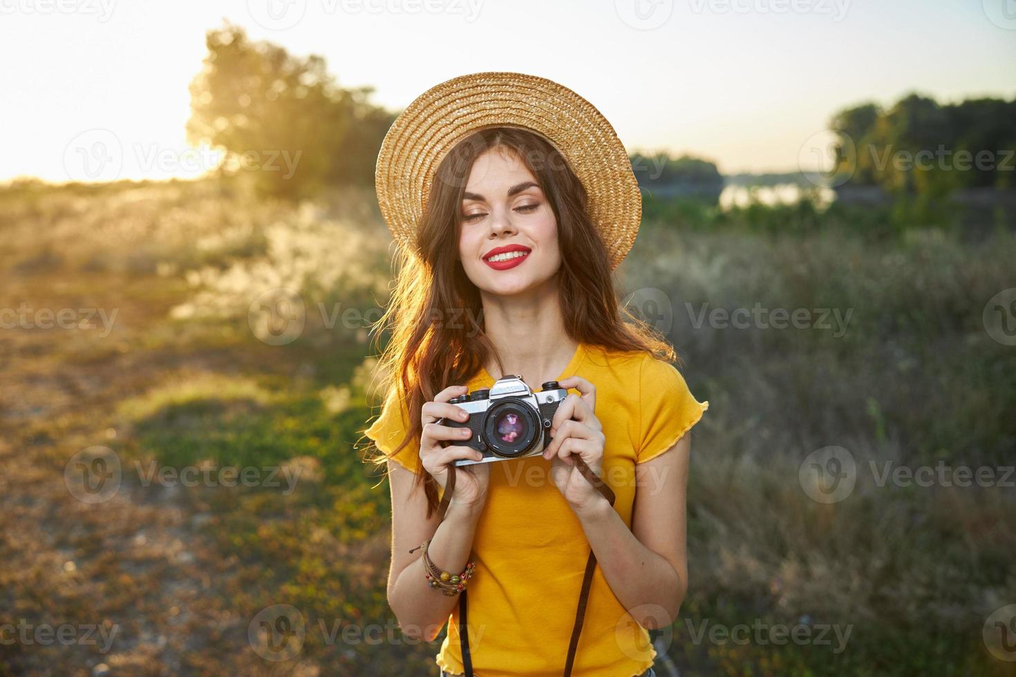 donna con chiuso occhi con un' telecamera nel sua mani indossare un' cappello rosso labbra natura sole stile di vita foto