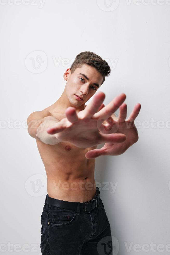 un' uomo con un' nudo torso gesti con il suo mani nel davanti di il suo viso su un' leggero sfondo foto