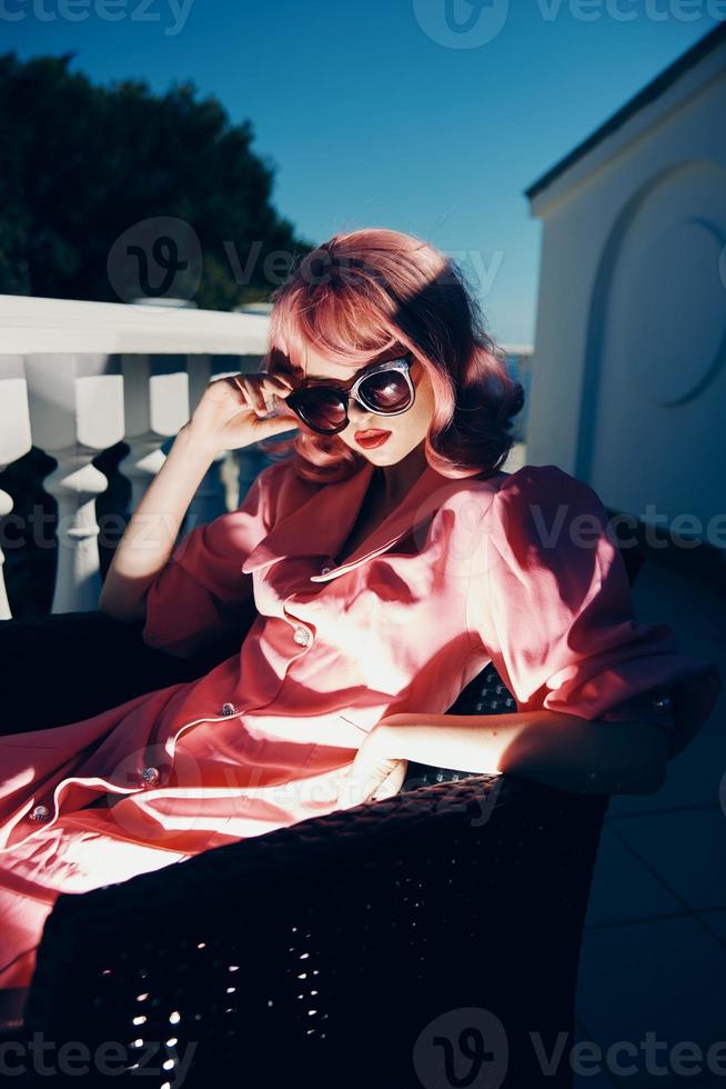 attraente donna rosa vestito si siede su il terrazza soleggiato giorno foto