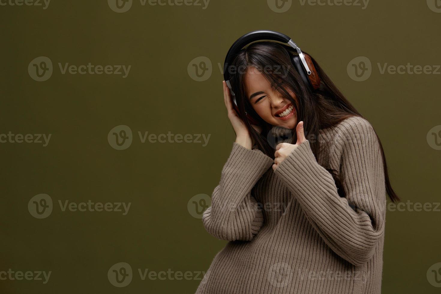 brunetta nel un' maglione ascoltando per musica con cuffie divertimento studio modello foto