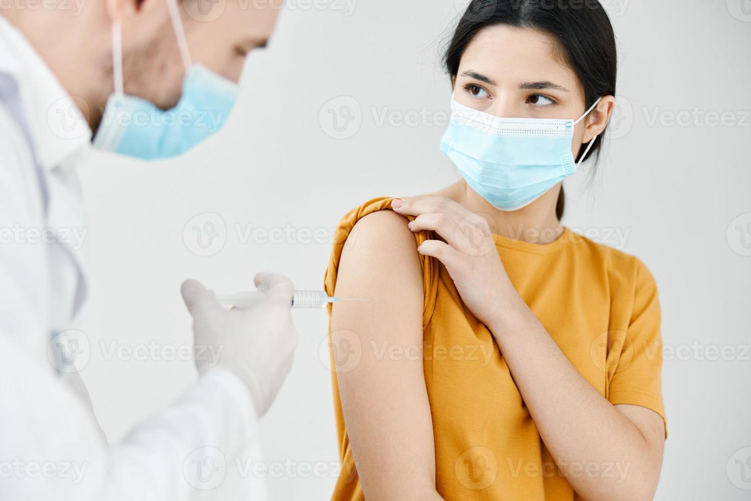 un' professionale medico nel un' bianca cappotto inietta un' vaccino in il spalla di un' donna nel un' medico maschera vaccinazione foto