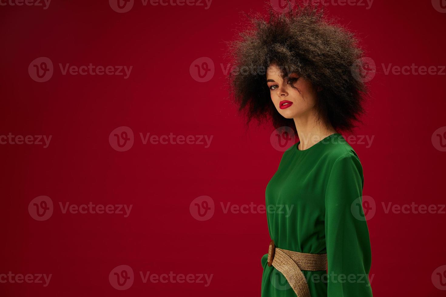 donna con un' lussureggiante Riccio acconciatura nel un' verde vestito rosso sfondo foto