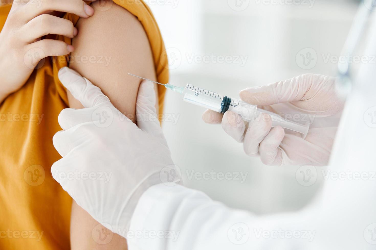 medico nel un' medico toga dando un' tiro per il spalla di un' donna nel un' giallo maglietta nel un' ospedale vaccinazione foto