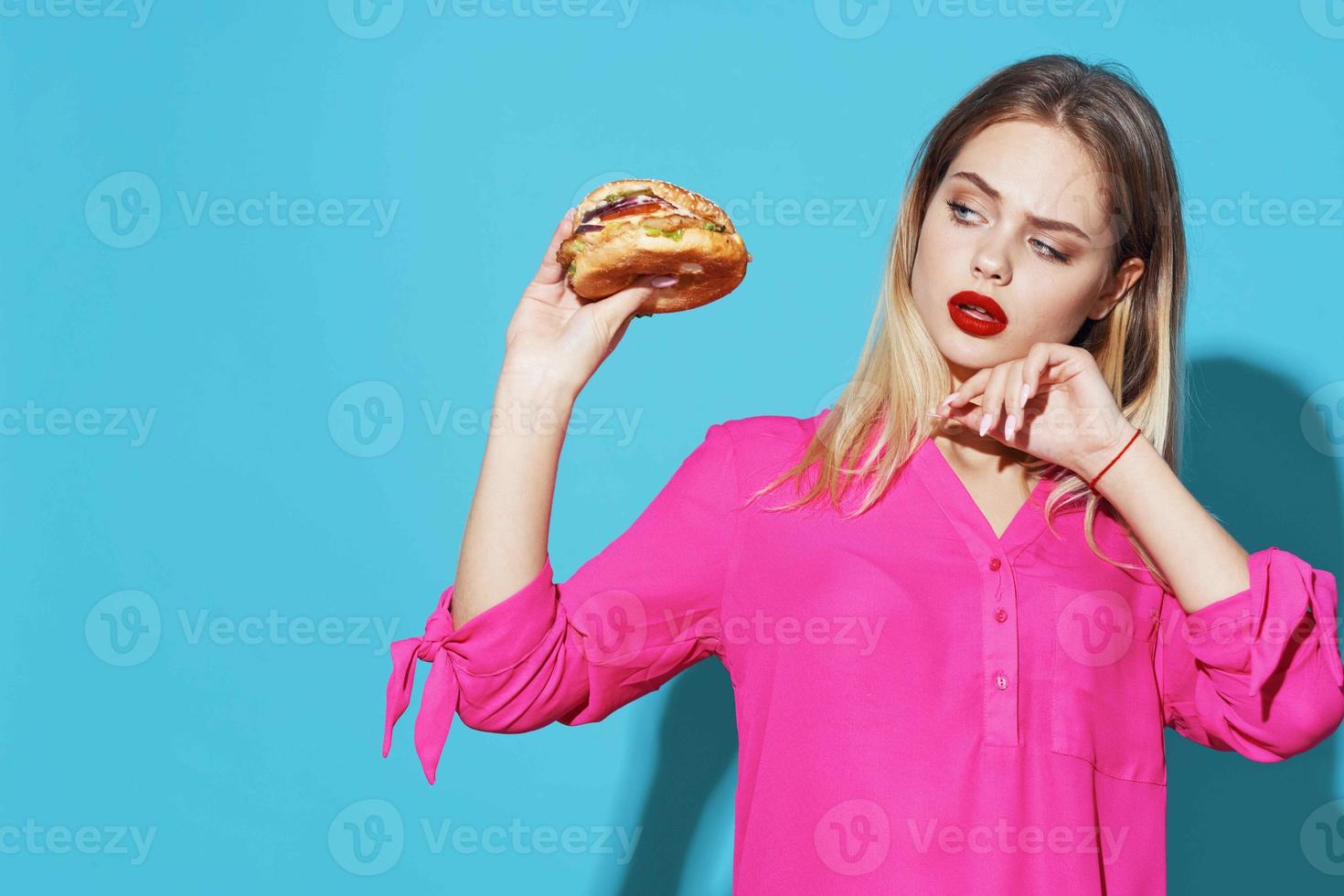 allegro bionda nel un' rosa camicia Hamburger veloce cibo merenda blu sfondo foto