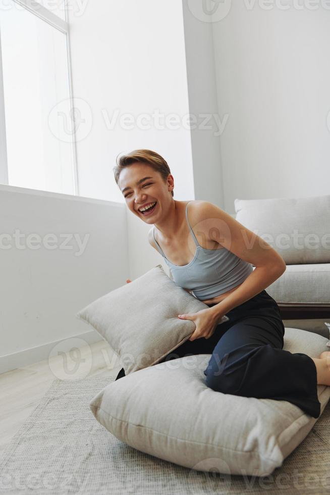 adolescenziale ragazza Sorridi tutti si siede a casa vicino il divano e lanci su cuscini, divertimento gioco e felicità senza filtri, copia posto foto