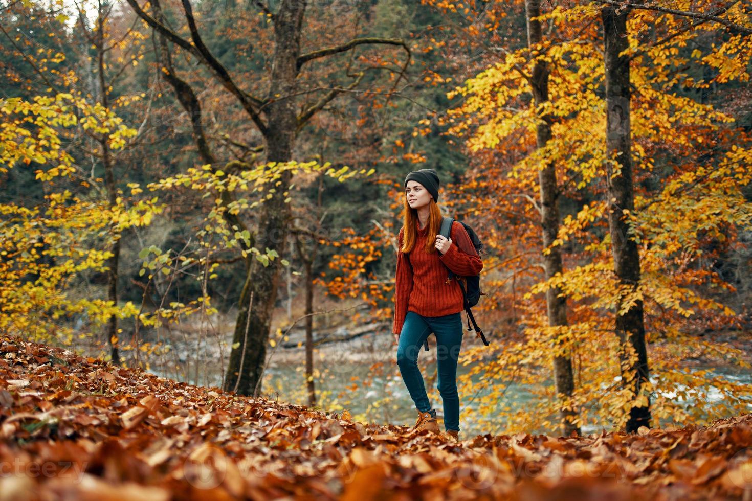 donna turista passeggiate attraverso il parco nel autunno con un' zaino su sua indietro e alto alberi paesaggio fiume lago foto