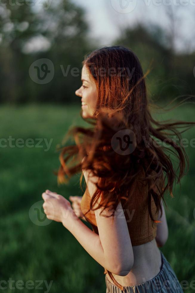 un' contento atletico donna è jogging e sorridente nel natura nel il parco, estate tramonto leggero foto