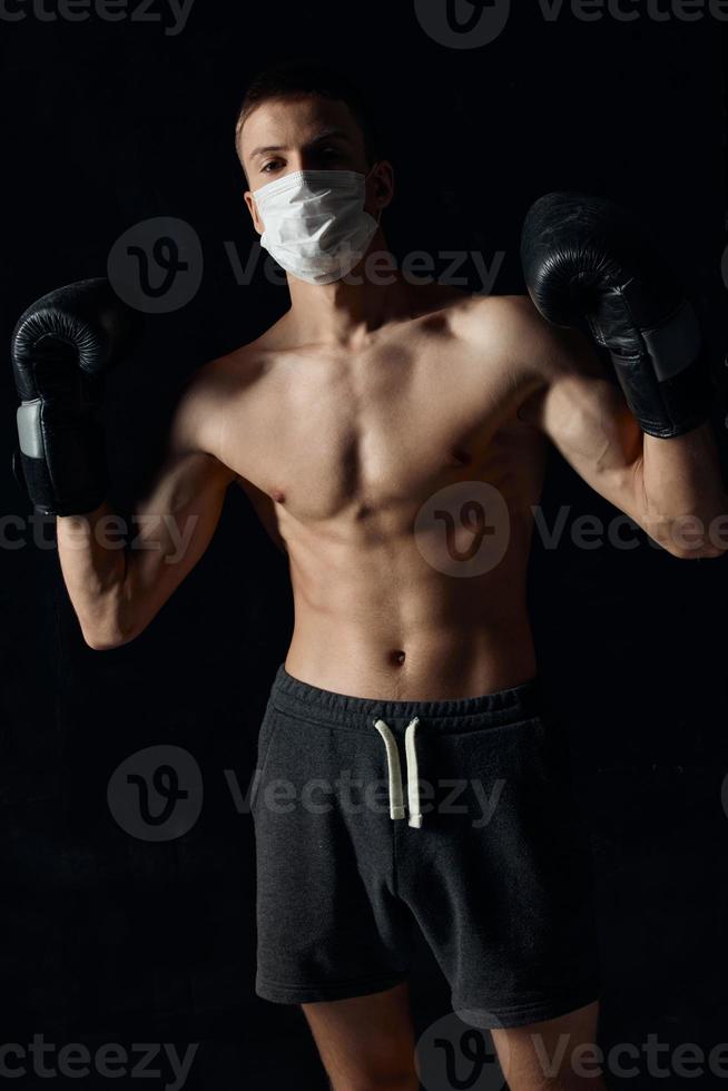 sportivo uomo nel medico maschera e nel boxe guanti su nero sfondo pantaloncini fitness modello stampa foto