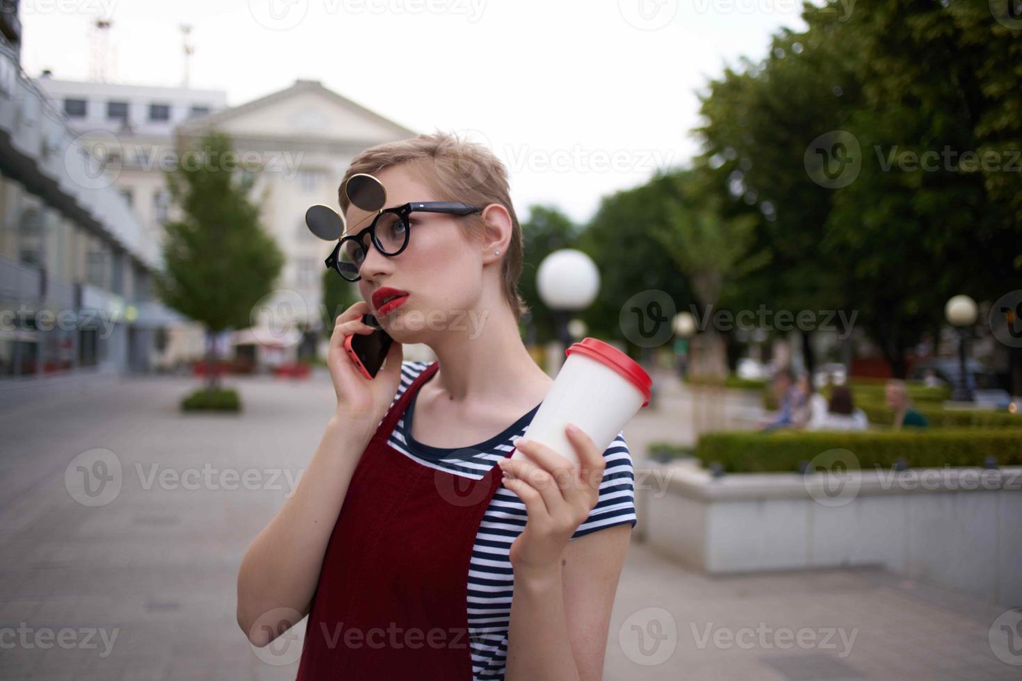 donna con bicchieri su il strada parlando su il Telefono nel un' bicchiere con un' bevanda foto