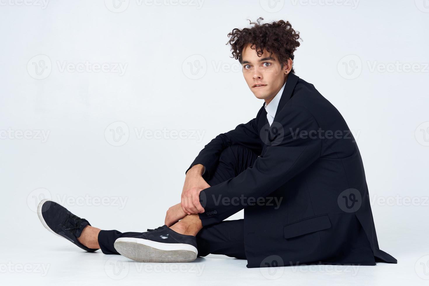 tipo con Riccio capelli nel un' completo da uomo seduta su il pavimento moda fiducia in se stessi foto