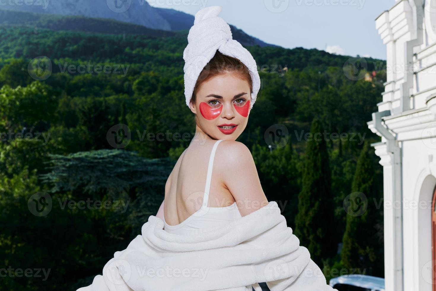 attraente giovane donna sta nel un' accappatoio contro il fondale di montagne con cerotti su il suo viso Perfetto soleggiato mattina foto