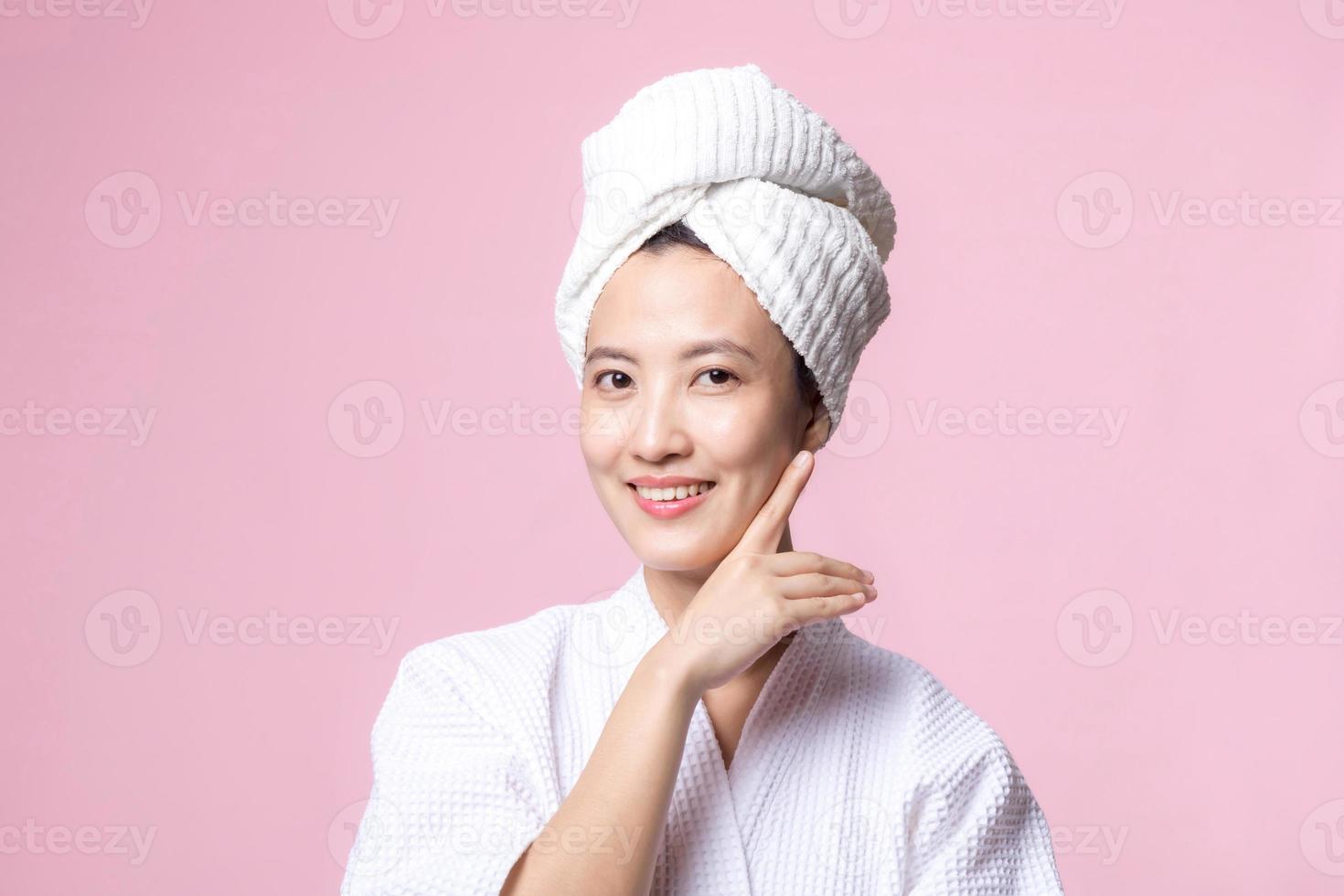 bellissimo giovane asiatico donna contento con pulito viso pelle nel asciugamano e accappatoio, terme completo da uomo su rosa sfondo. cura della pelle, trattamento, benessere terapia, facciale cura, bellezza femmina Salute, cosmetologia concetto foto