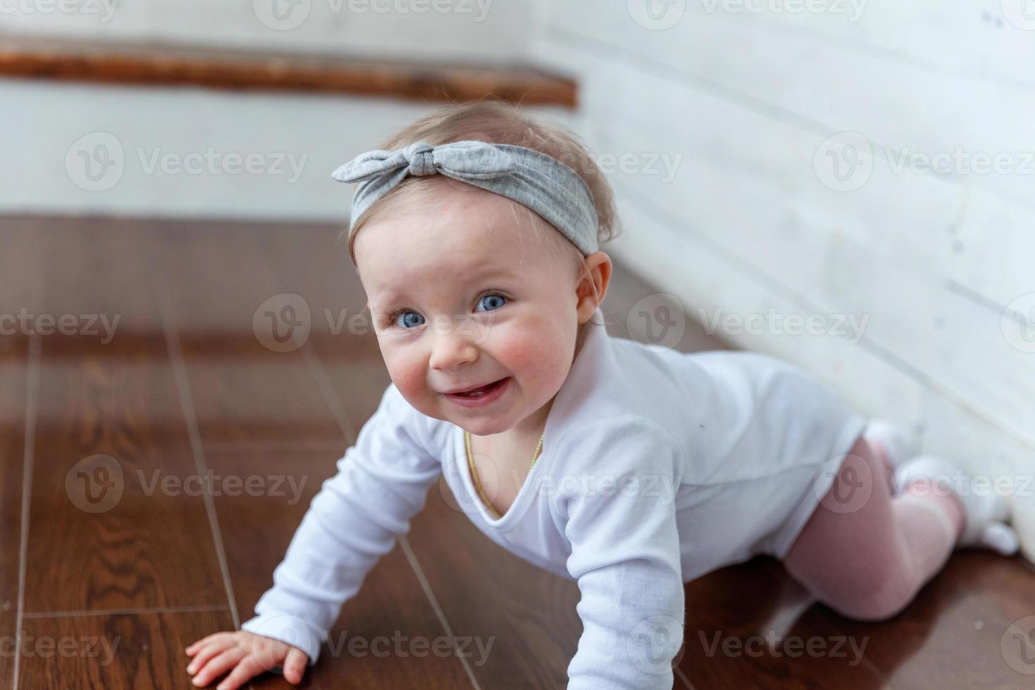 poco strisciando bambino ragazza uno anno vecchio ubicazione su pavimento nel luminosa leggero vivente camera vicino finestra sorridente e ridendo foto