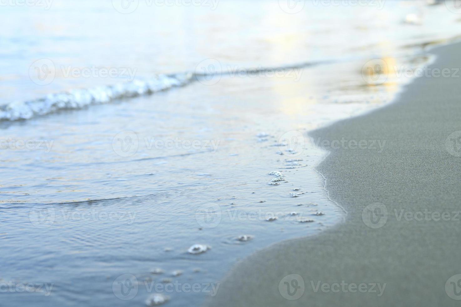 onda sfocata del mare sulla spiaggia di sabbia di sera foto