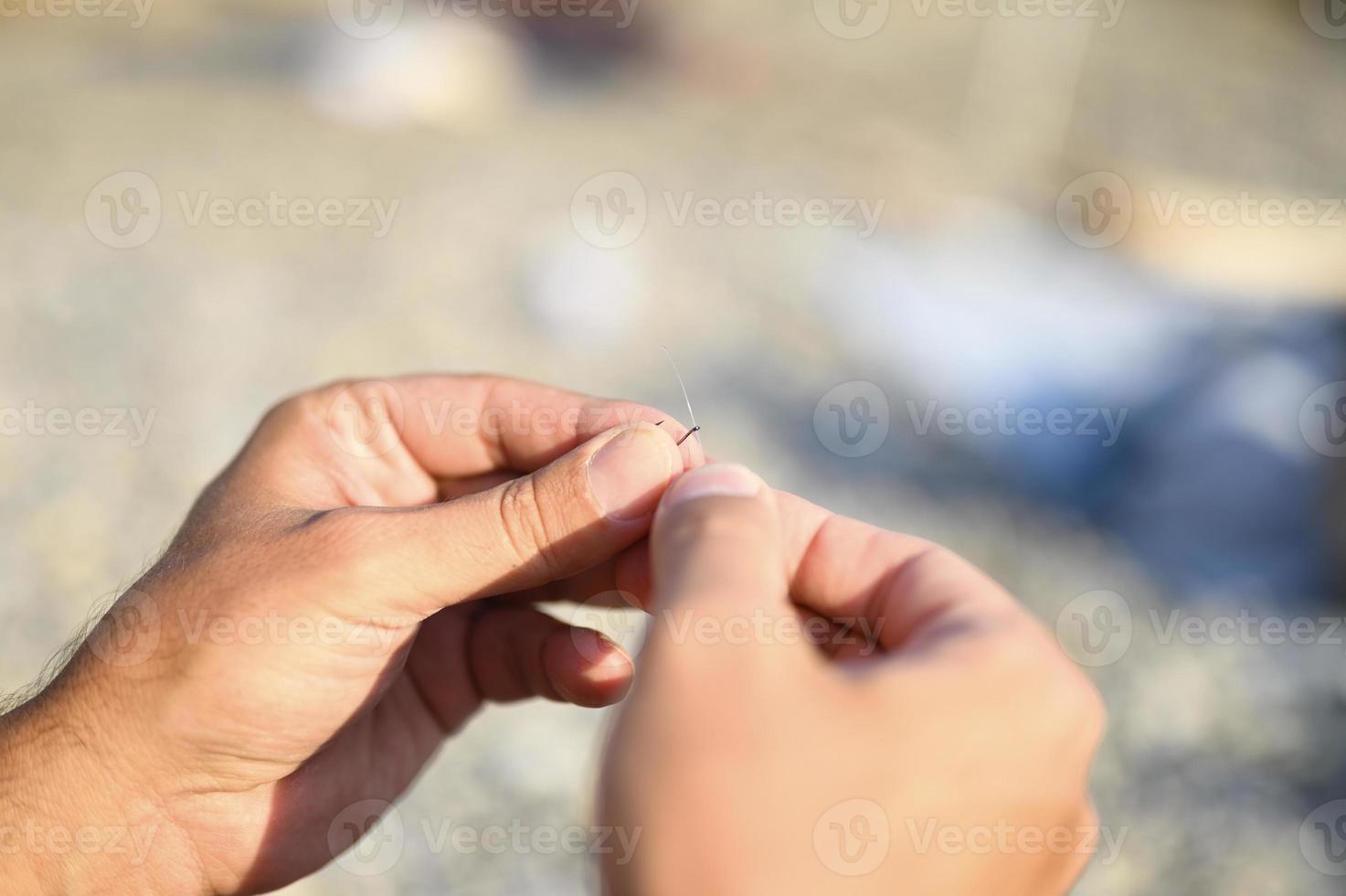 mani dell'uomo che lega una lenza su un amo da pesca foto