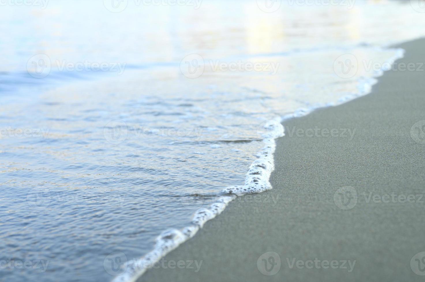 onda sfocata del mare sulla spiaggia di sabbia di sera foto