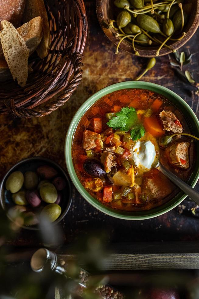 zuppa di carne solyanka cucinata in casa servita con pane, olive e capperi foto
