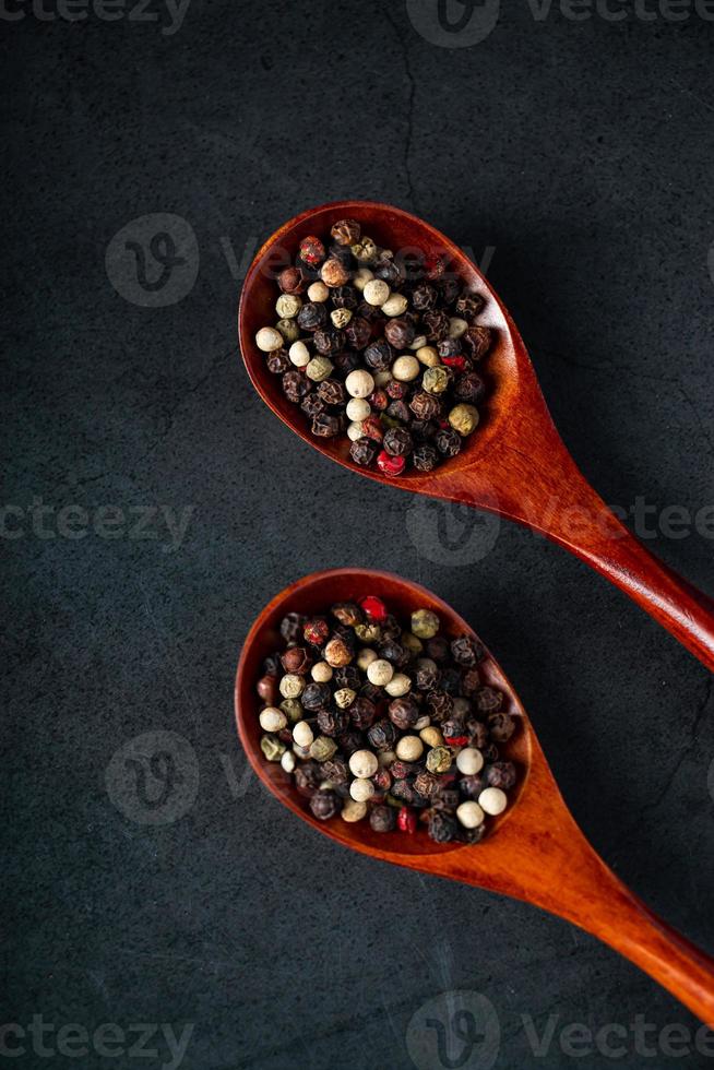 mix di pepe rosso e nero in cucchiaio di legno su sfondo nero foto