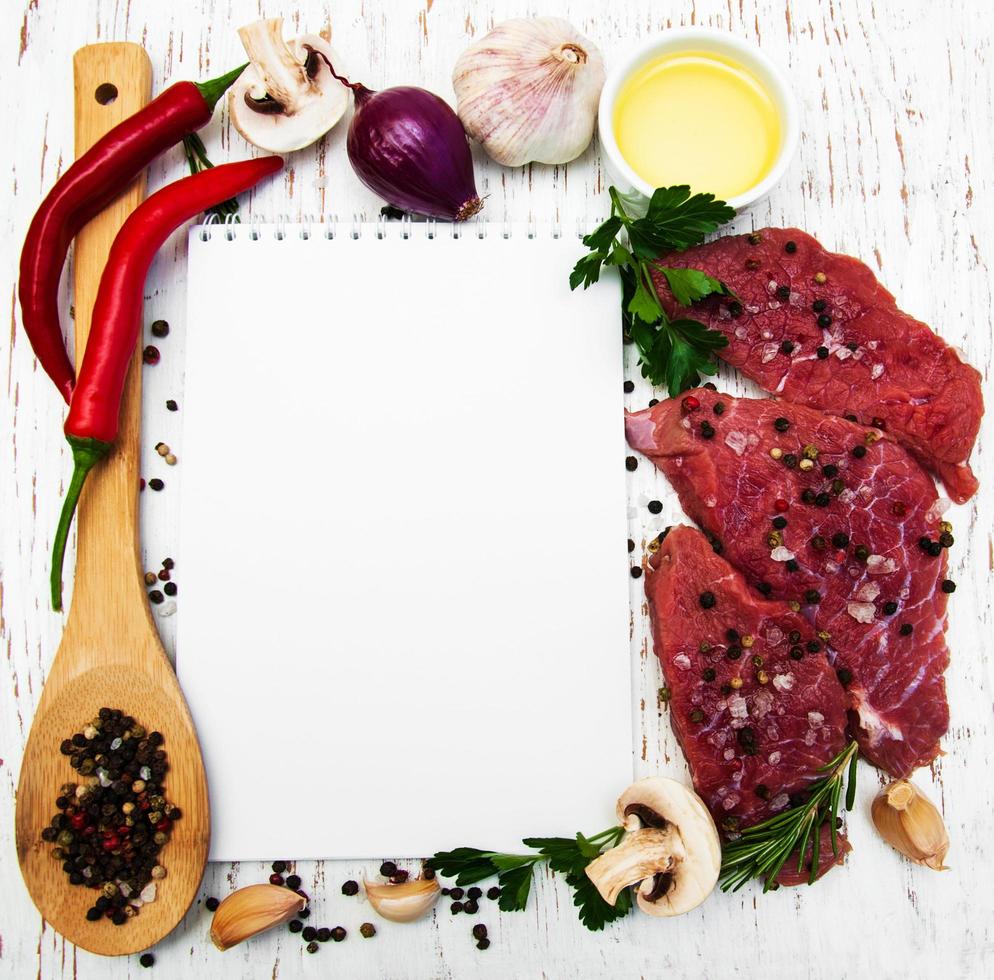 bistecche di carne, un ricettario e ingredienti su un vecchio fondo di legno foto