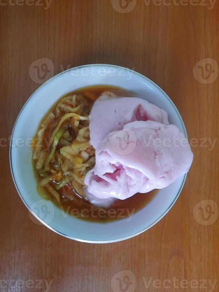 un' rujak o speziato frutta insalata piatto sormontato con fragola ghiaccio crema foto