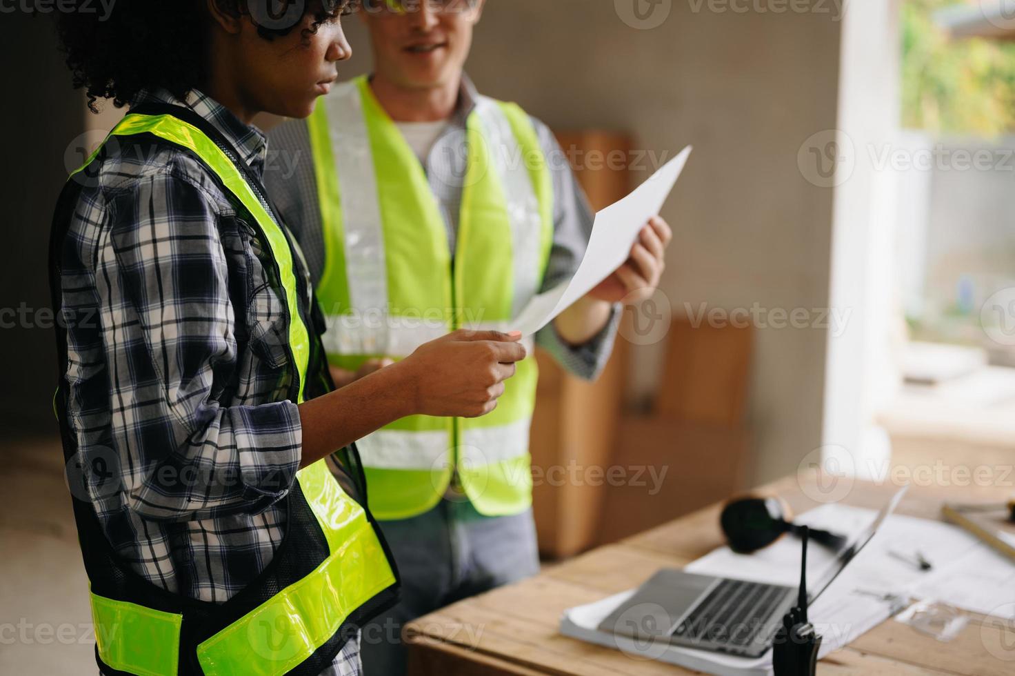 contraente e architetto guardare a Piano, tavoletta, il computer portatile e parlando di Lavorando su grande progetto. edificio nel costruzione processi interno. squadra opera foto