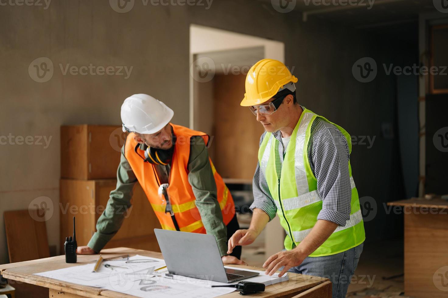 contraente e architetto guardare a Piano, tavoletta, il computer portatile e parlando di Lavorando su grande progetto. edificio nel costruzione processi interno. squadra opera foto