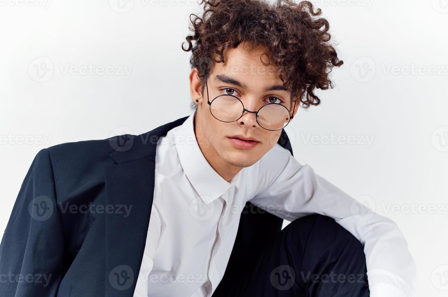 avvicinamento ritratto di bello tipo con Riccio capelli indossare bicchieri e nel un' classico completo da uomo foto