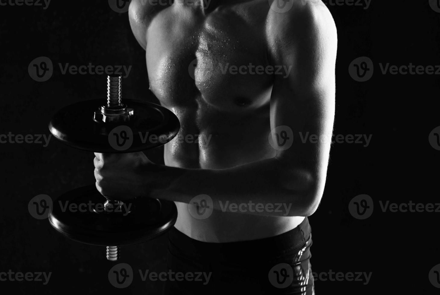 uomo con manubri nel il suo mani nudo muscolare corpo allenarsi buio sfondo foto