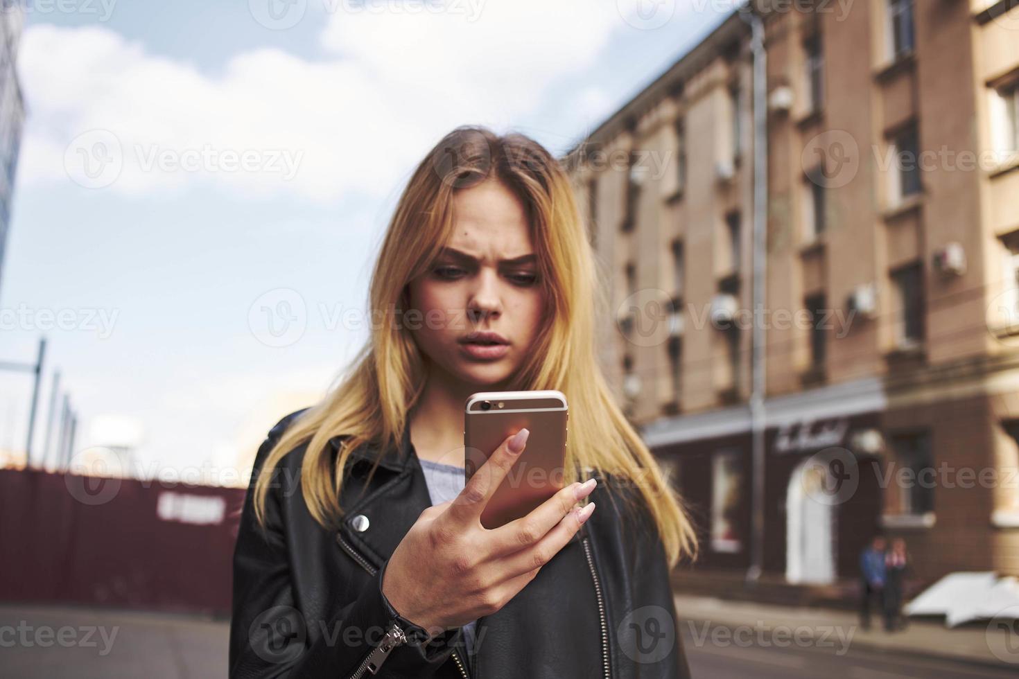 ritagliata Visualizza di bionda donna con mobile Telefono su il strada vicino il edificio foto