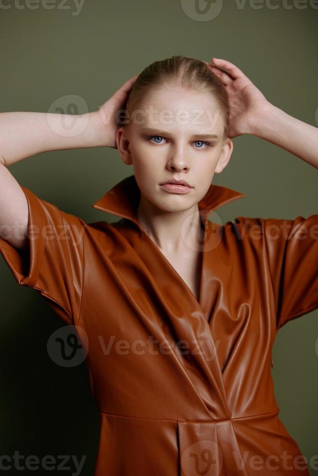 grave fiducia giovane bionda ragazza con coda di cavallo nel elegante pelle vestito sembra a telecamera toccante testa in posa isolato per mercato striscione. studio ritratto su verde sfondo. rivendita concetto foto