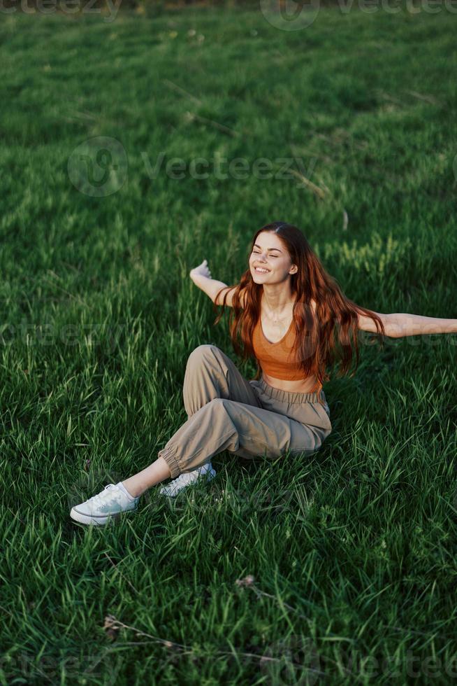 un' donna godendo il all'aperto seduta nel il parco su il verde erba nel casuale capi di abbigliamento con lungo fluente capelli, illuminato di il luminosa estate sole senza zanzare foto