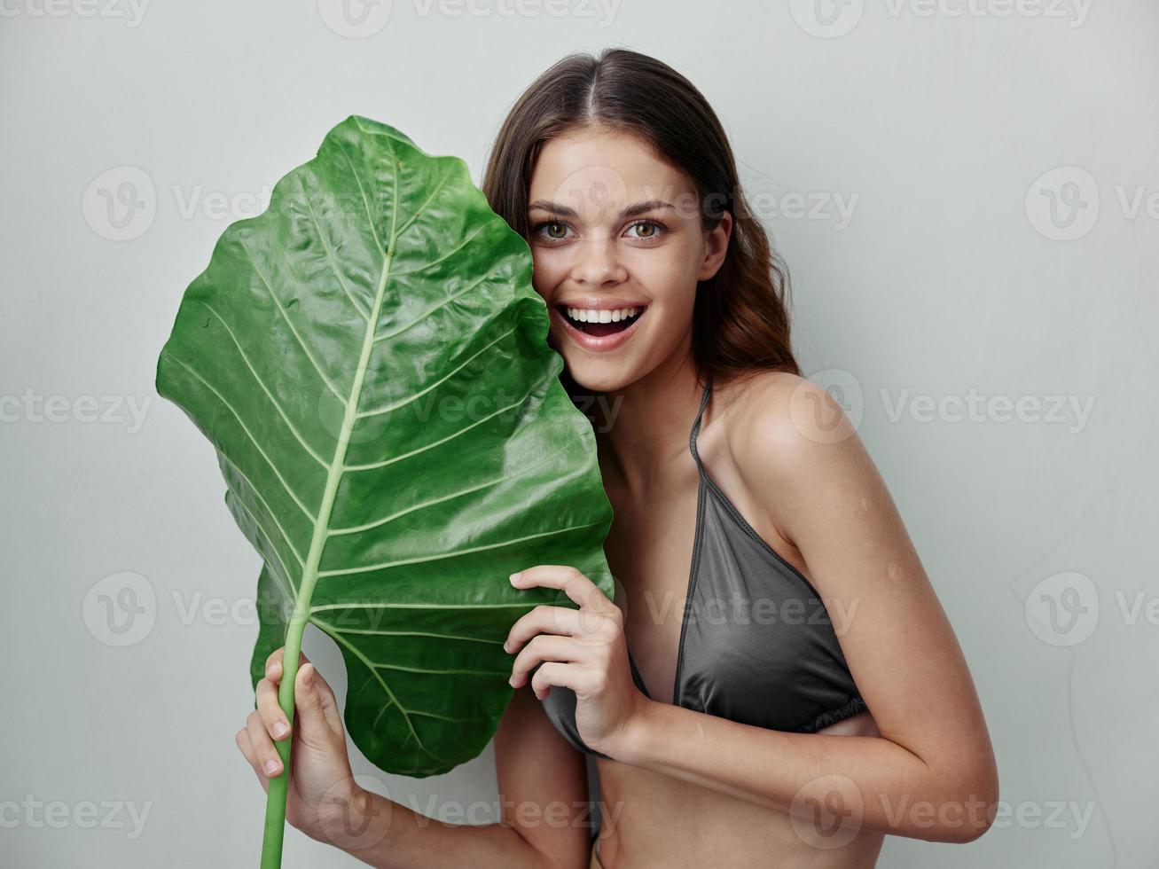 allegro donna nel grigio costume da bagno con palma foglia nel sua mani isolato sfondo foto