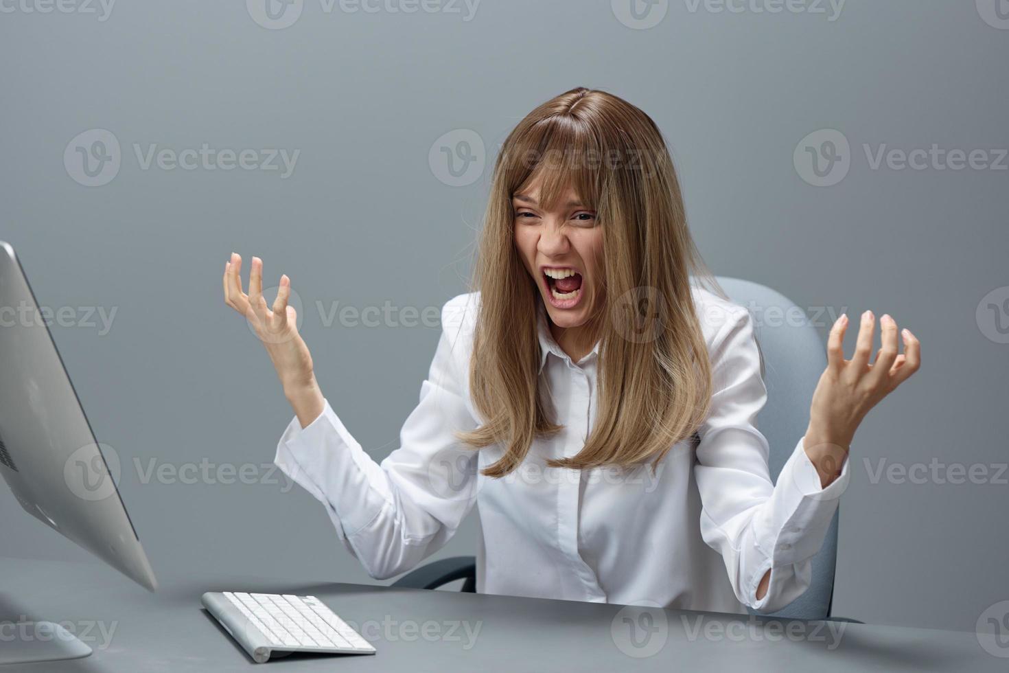 irritata bionda donna d'affari fatto un' critico sbaglio utilizzando del desktop computer diffusione mani seduta a posto di lavoro nel grigio moderno ufficio. a distanza lavoro, tecnologia e carriera professione concetto. copia spazio foto