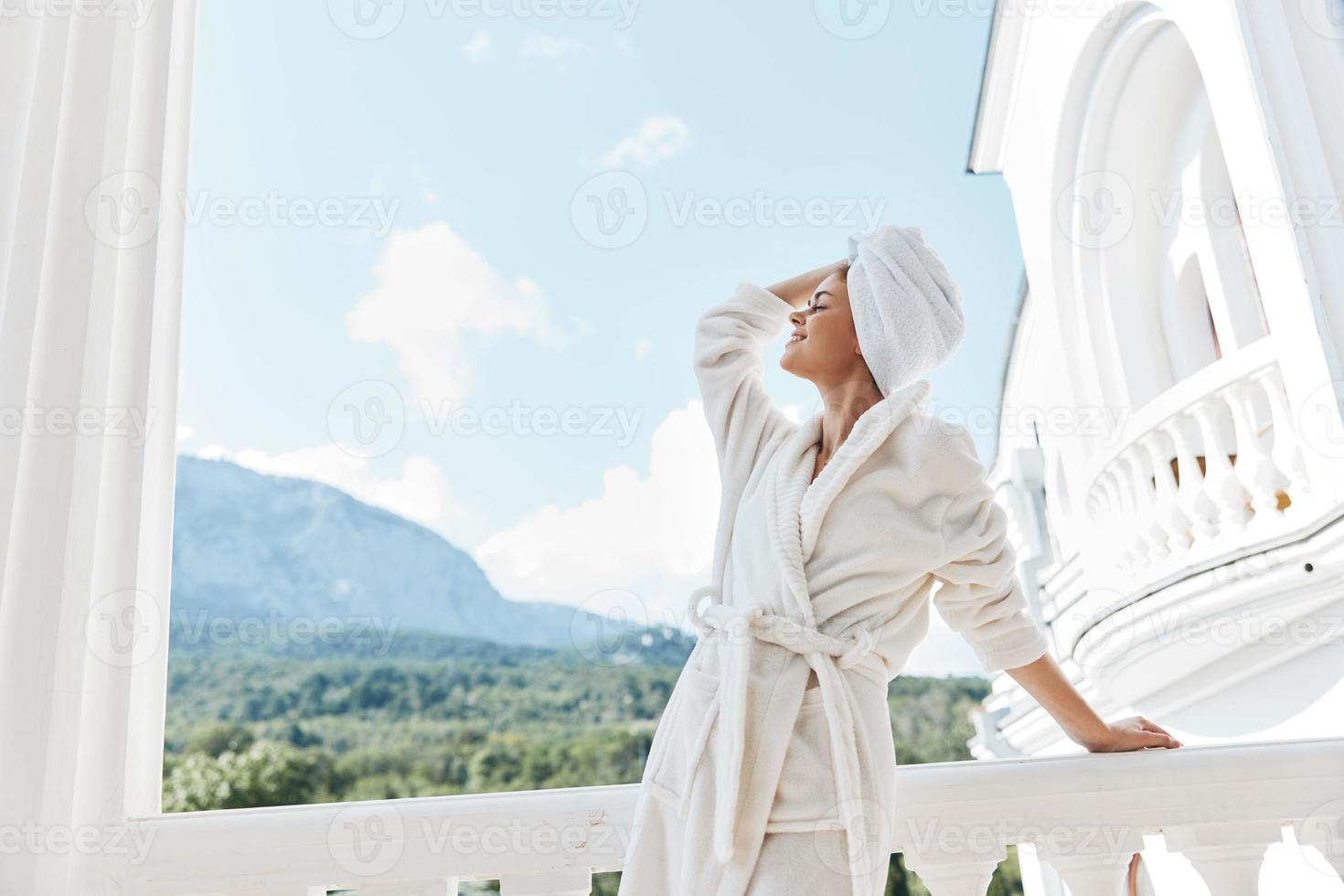 ritratto di bellissima donna con un' asciugamano su mio testa nel un' bianca accappatoio soggiorno su il balcone nel un' Hotel inalterato foto