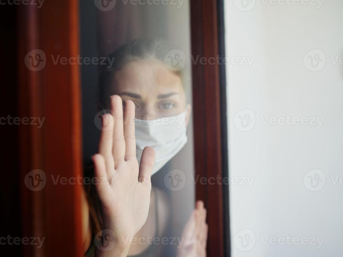 mascherato donna guardare su il finestra avvicinamento bandire foto