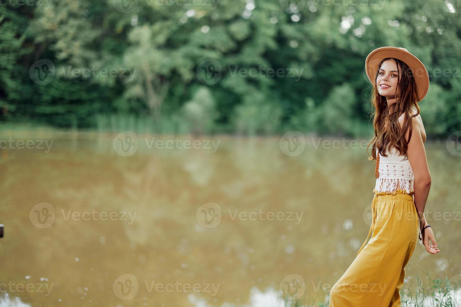 un' giovane donna nel un' hippie Guarda viaggi nel natura di il lago indossare un' cappello e giallo pantaloni nel il autunno foto