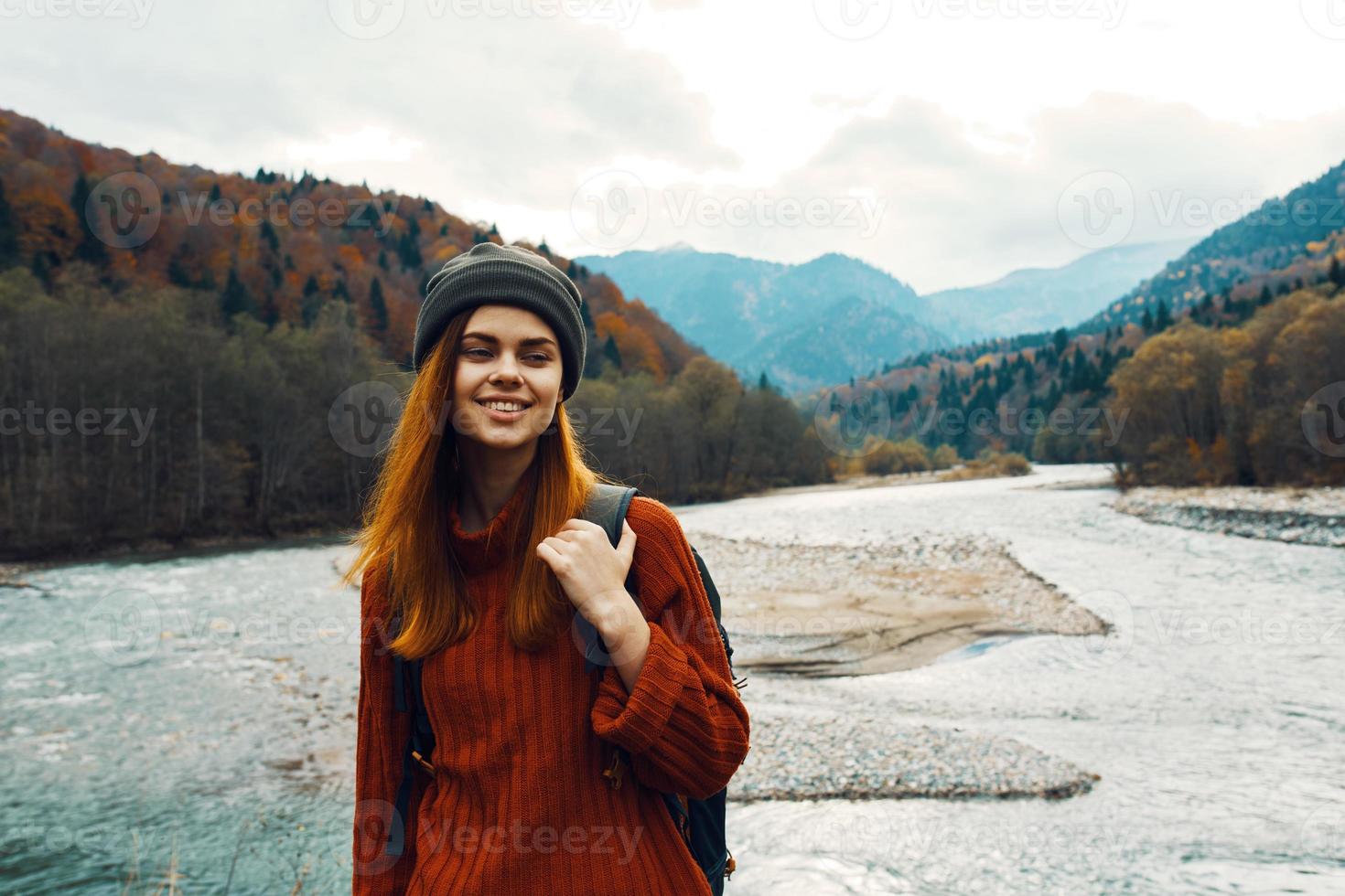 bellissimo donna nel un' maglione con un' zaino nel il montagne vicino il fiume nel natura ritratto foto