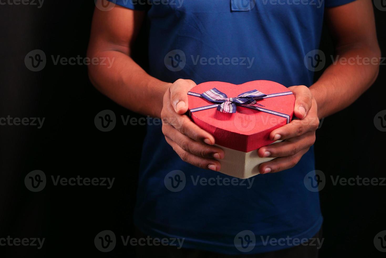 uomo con scatola regalo a forma di cuore isolato su sfondo nero foto