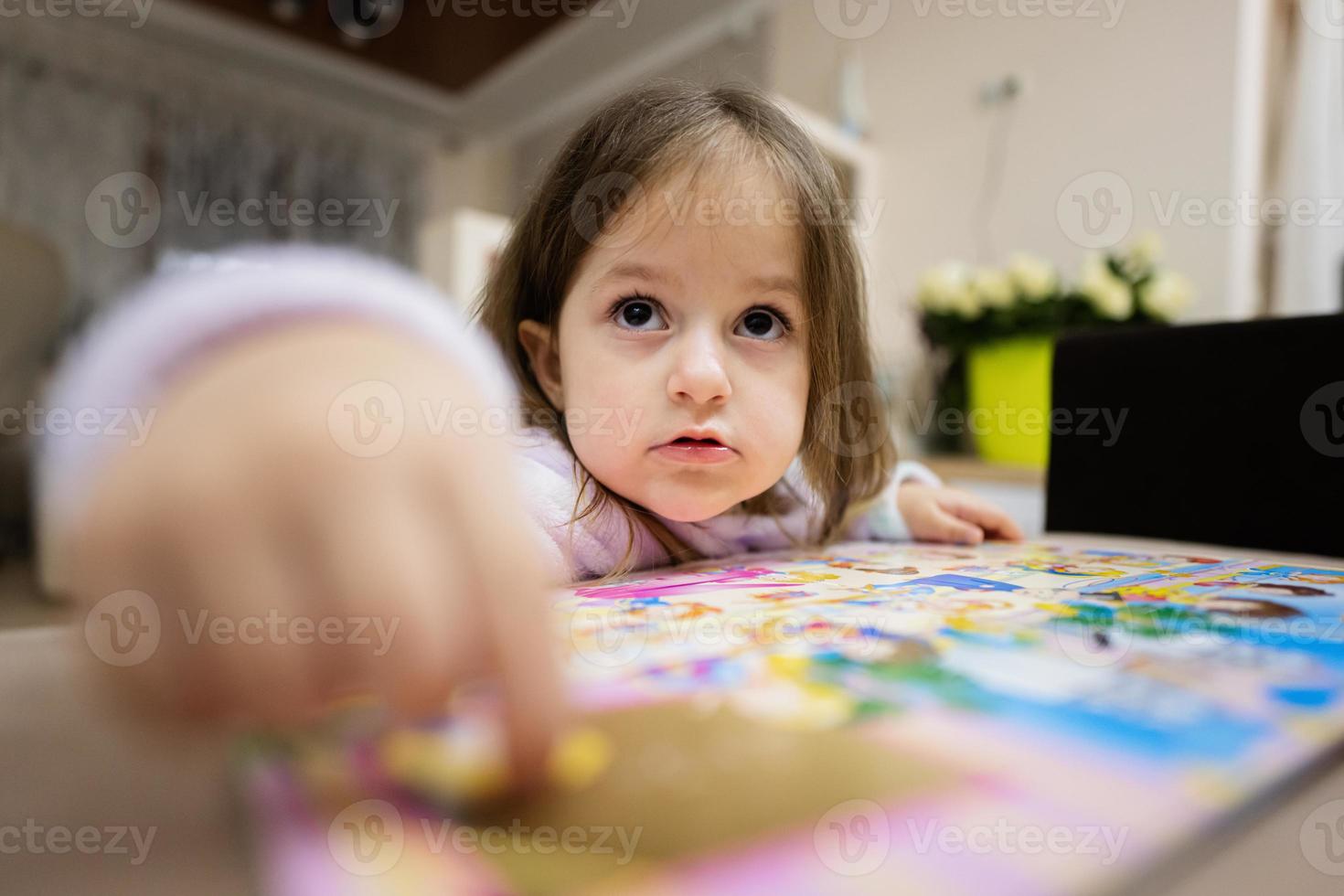 carino bambino ragazza nel pigiama guardare su libro a casa. foto