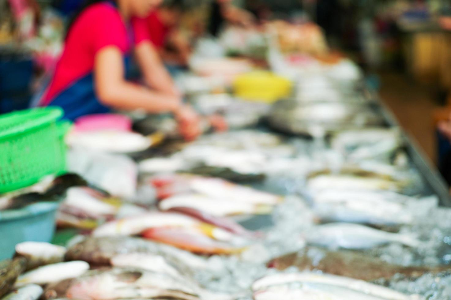 immagine sfocata di pesce fresco crudo sul vassoio per la vendita sul mercato con venditore sfocato foto