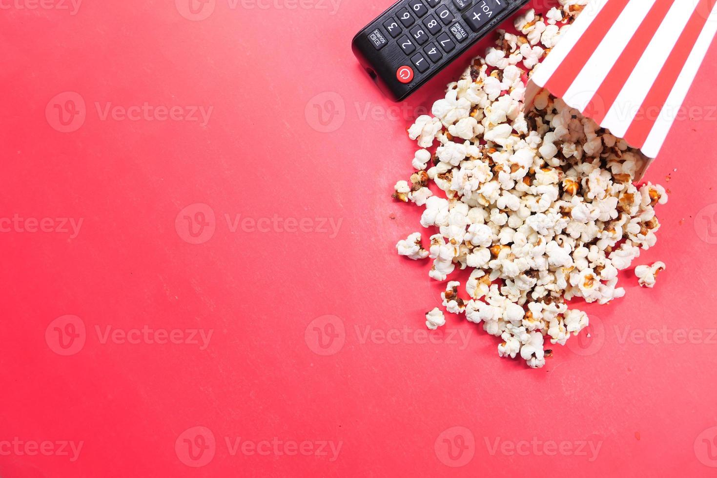 popcorn e telecomando della tv su sfondo rosso foto