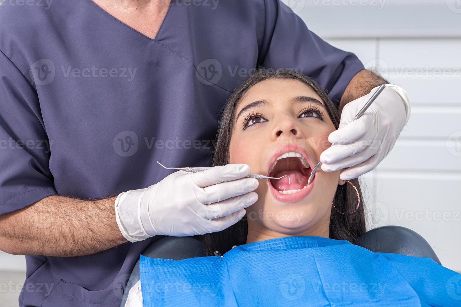 Ritaglia dentista ispezionando ha aperto bocca di adolescente foto