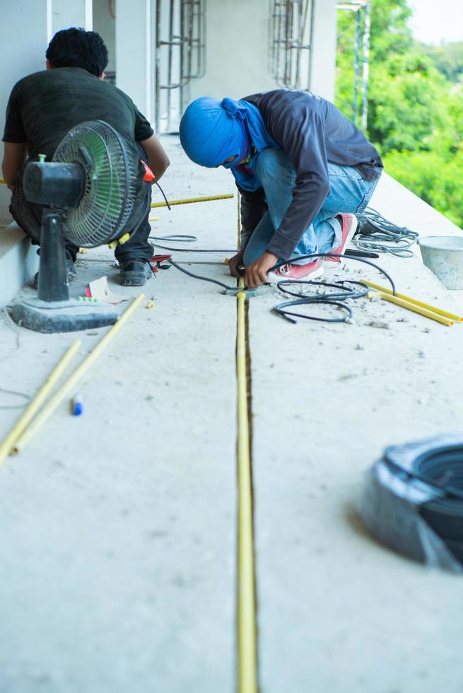 lavoratori che installano il cavo elettrico e il tubo nella casa in costruzione foto