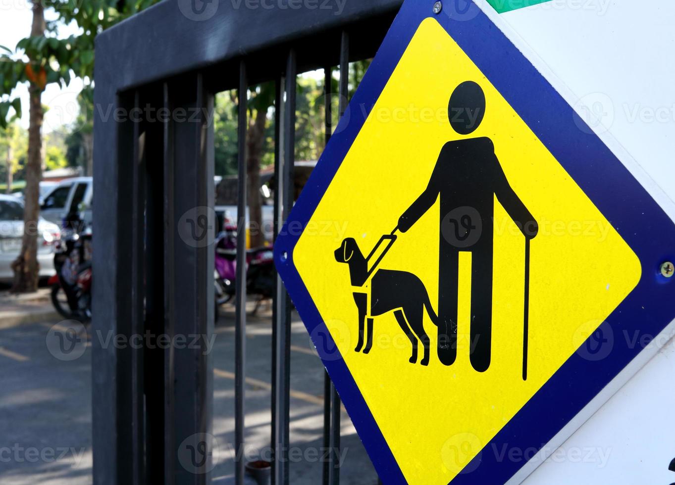 cieco uomo e cane cartello su giallo piazza forma piatto sospeso su dipinto nero metallo porta di pubico parco. accanto Visualizza. foto