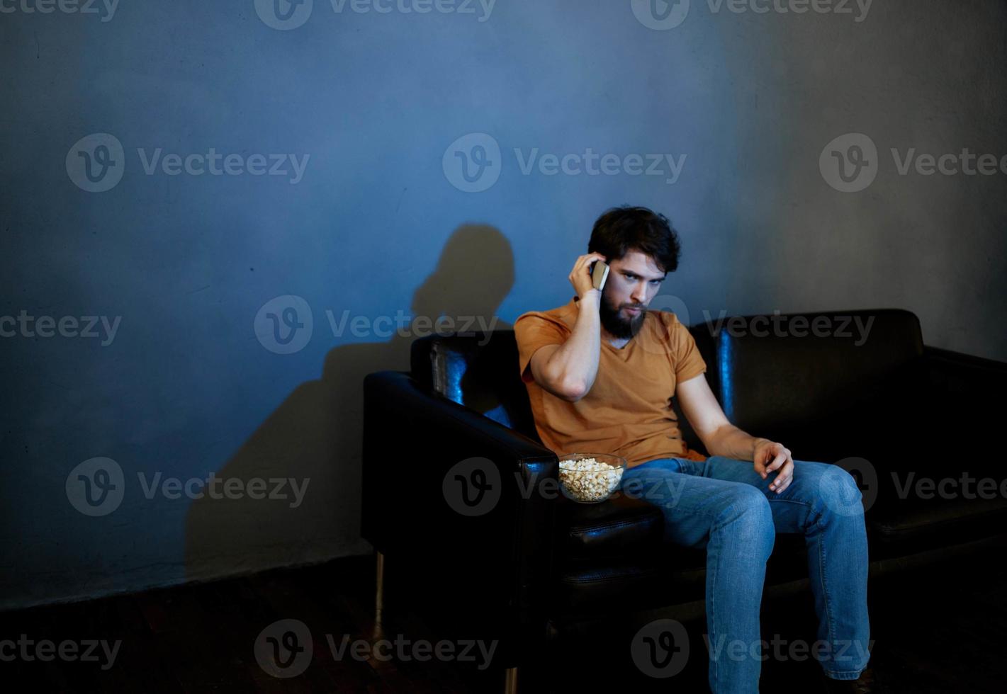 solitario uomo nel il sera su il divano nel davanti di il tv e Popcorn nel un' piatto foto